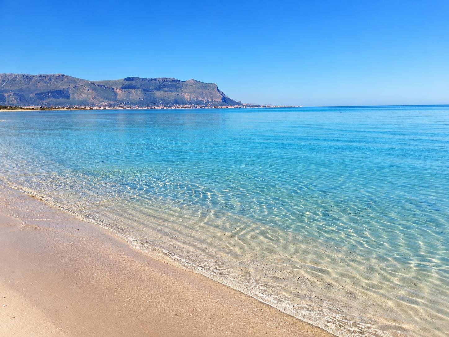 Turquoise water and sandy beach at Isola delle Femmine with Capo Gallo behind