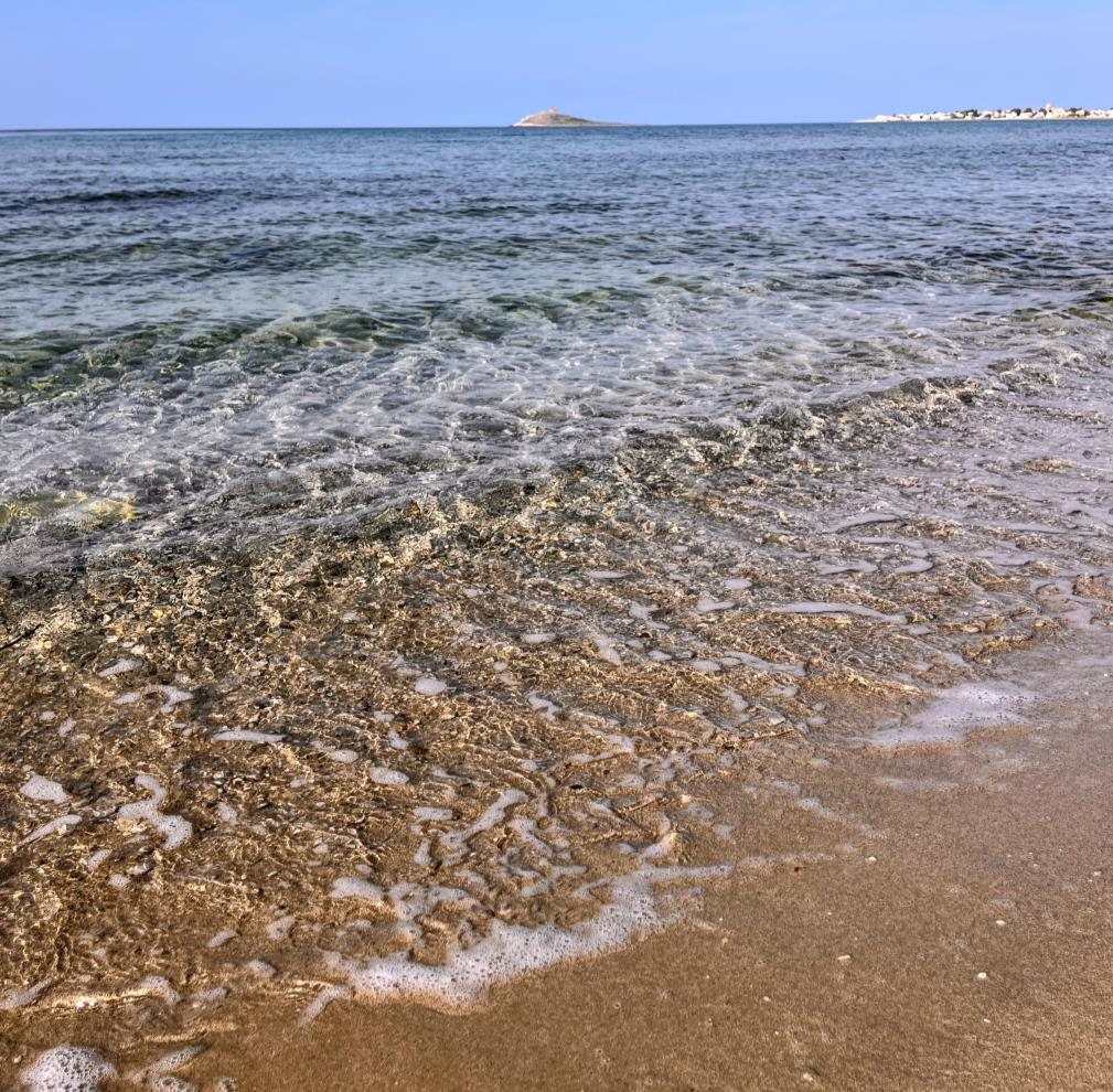 Waves on the sandy shoreline with the islet in the distance